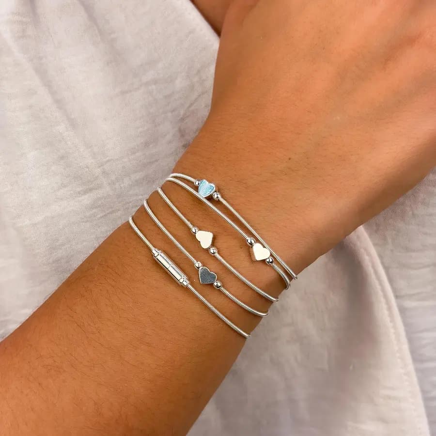 Pulseiras corda de violão prateadas com coração, uma delas com coração azul, no pulso de uma modelo