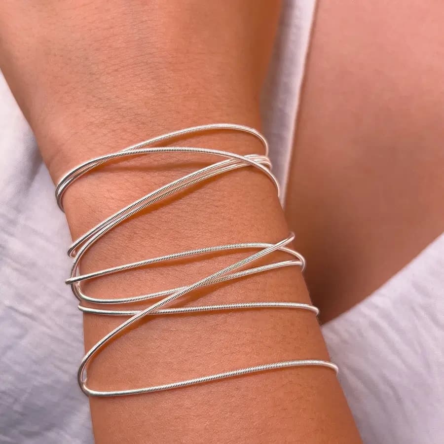 Pulseiras corda de violão prateadas lisas, cruzadas no pulso de uma modelo