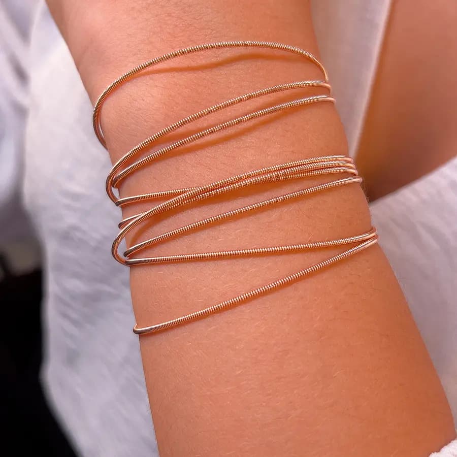 Pulseiras corda de violão cor rosê lisas, cruzadas no pulso de uma modelo