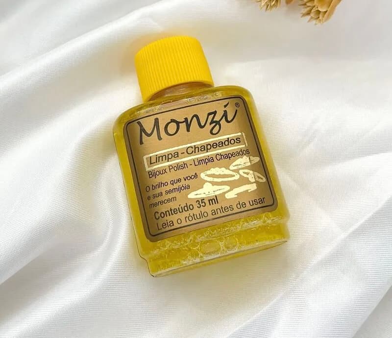Frasco de 35 ml do Monzi Limpa Chapeados, líquido amarelo com tampa amarela, sobre cetim branco