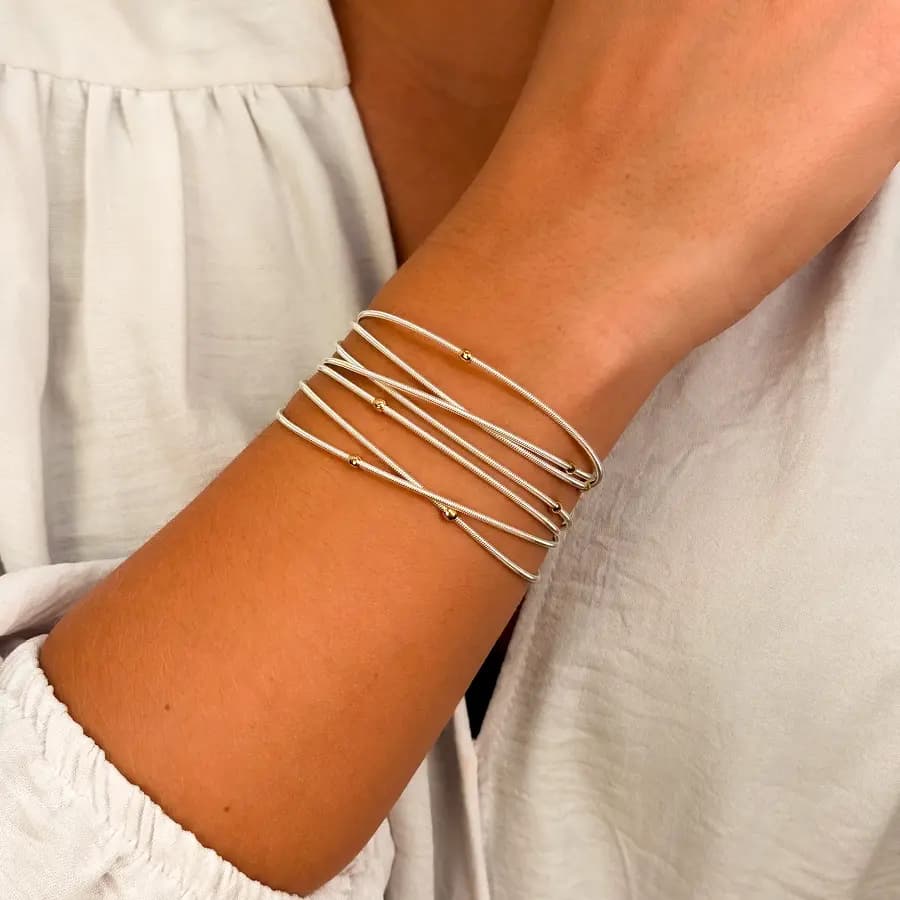Pulseiras corda de violão prateadas com bolinhas douradas no pulso de uma modelo