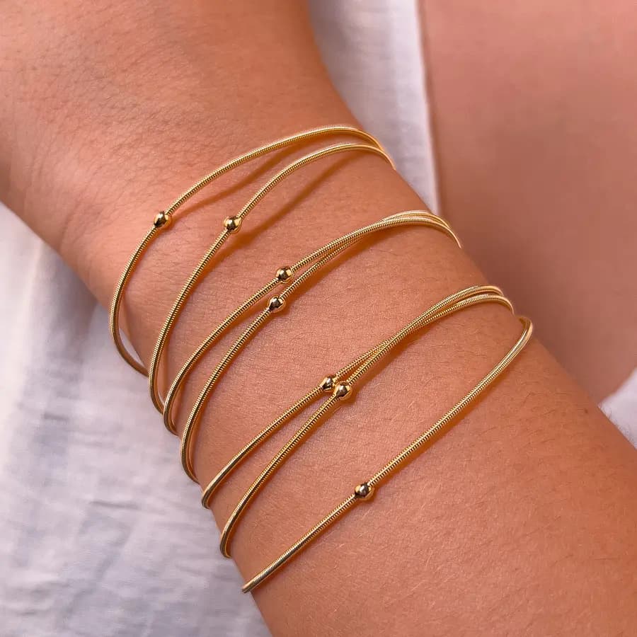 Pulseiras corda de violão douradas com bolinhas douradas no pulso de uma modelo