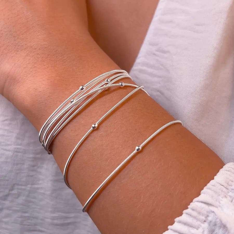 Pulseiras corda de violão prateadas com bolinhas de prata no pulso de uma modelo