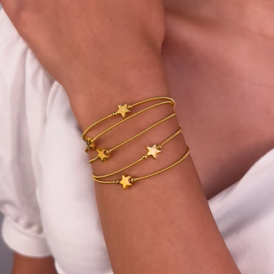 Pulseiras corda de violão douradas com estrela, empilhadas no braço de uma modelo