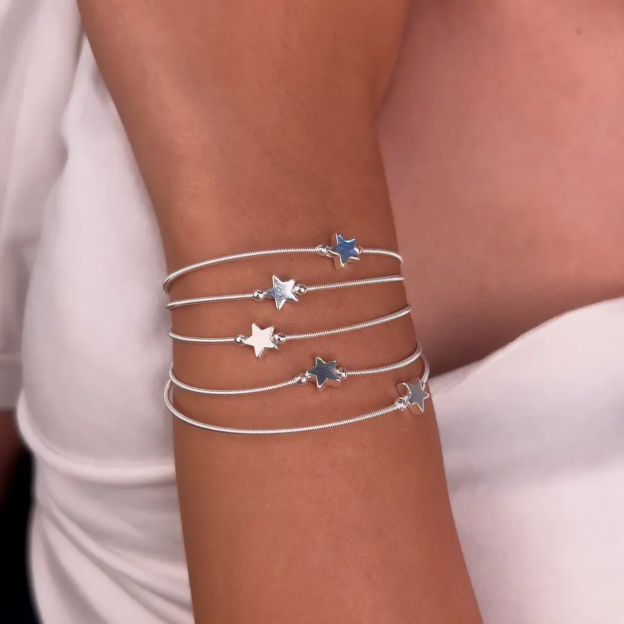 Pulseiras corda de violão prateadas com estrela, empilhadas no braço de uma modelo