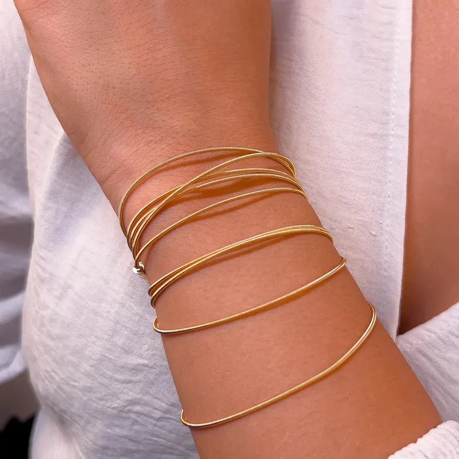 Pulseiras corda de violão douradas lisas, cruzadas no pulso de uma modelo