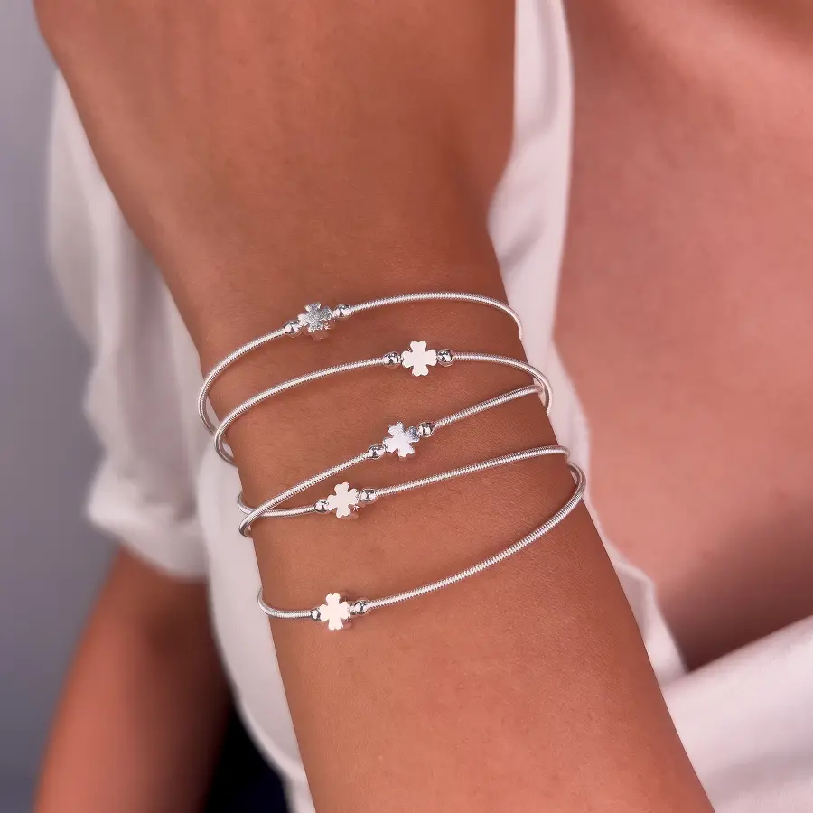 Pulseiras corda de violão prateadas com trevo de quatro folhas, empilhadas no pulso de uma modelo